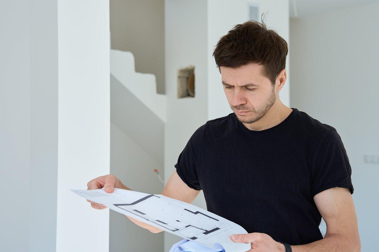 Un property manager examine attentivement des plans de travaux dans un appartement en rénovation.